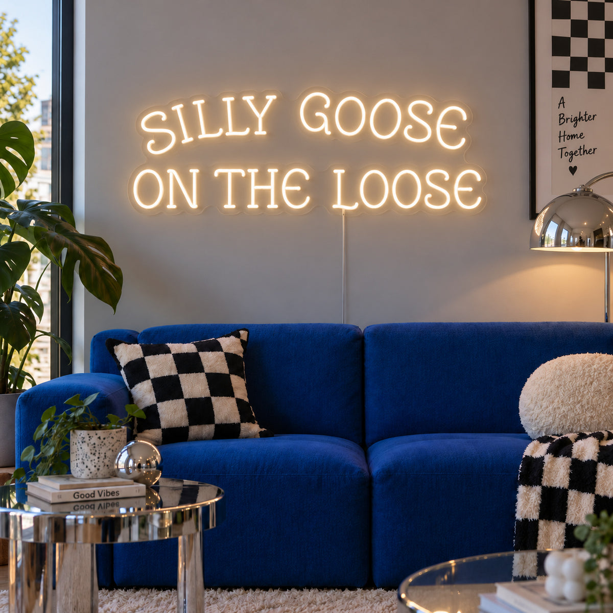 Warm White version of the Silly Goose On The Loose Neon Sign, shown above a blue sofa with checkered cushions.