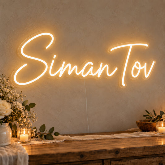 Siman Tov Neon Sign on clear cut-to-shape acrylic, illuminated on a wall in a styled celebration setting