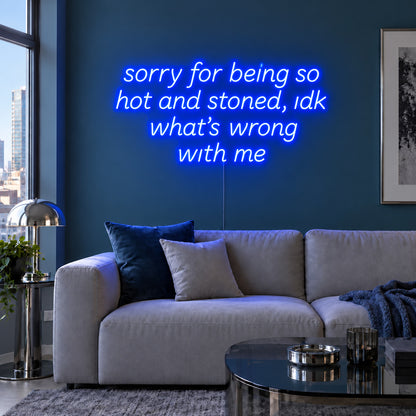 Sorry For Being So Hot And Stoned, Idk What's Wrong With Me Neon Sign glowing blue above a grey sofa against a blue wall.