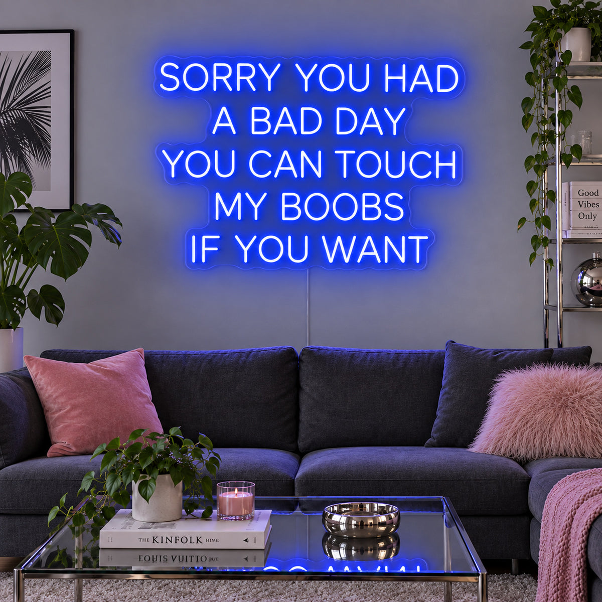 Sorry You Had A Bad Day You Can Touch My Boobs If You Want Neon Sign glowing blue above a grey sofa with pink cushions.