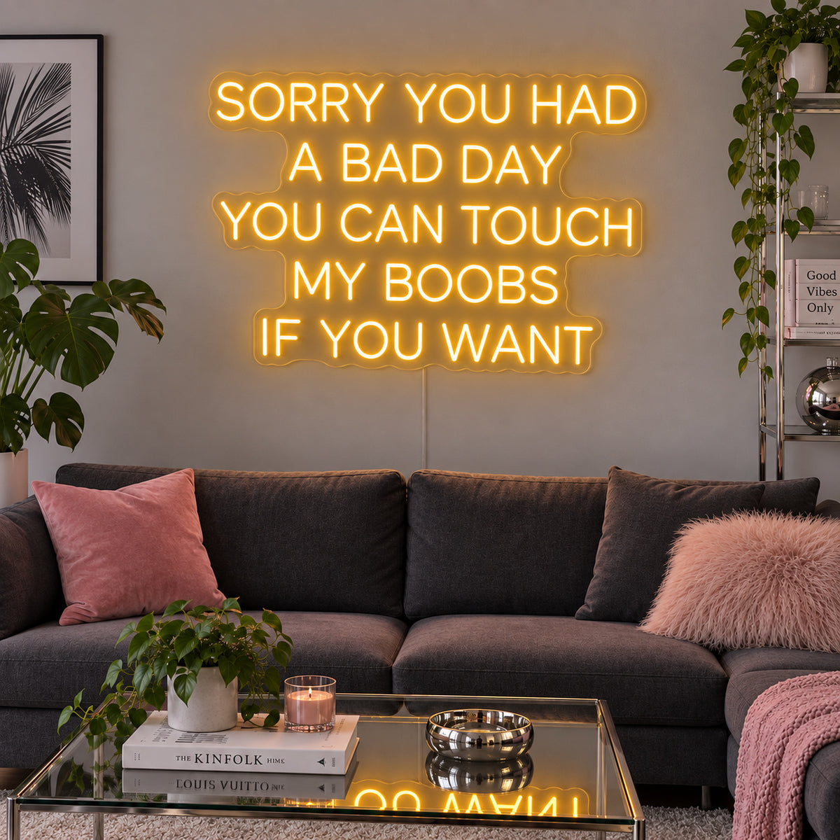 Sorry You Had A Bad Day You Can Touch My Boobs If You Want Neon Sign glowing gold above a grey sofa with pink cushions.