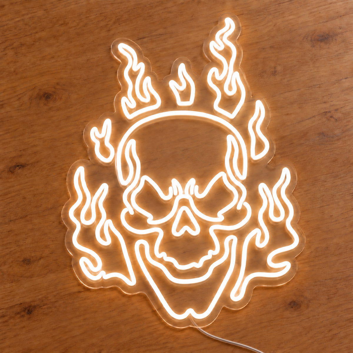 White Flaming Skull Neon Sign featuring a white skull surrounded by curling white flames, illuminated on clear acrylic lying on a natural oak wooden surface.